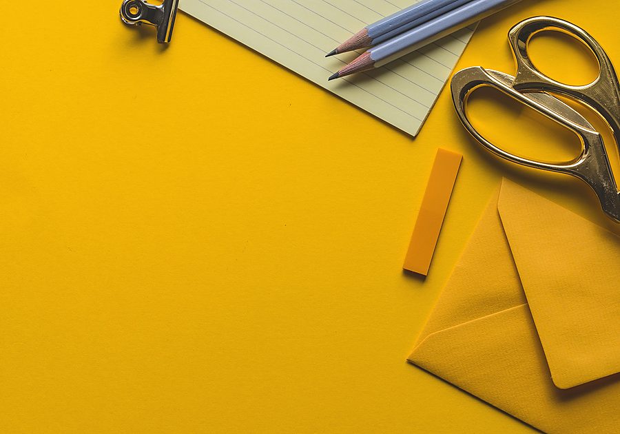 Notepad, pencils and scissors arranged on a yellow desk